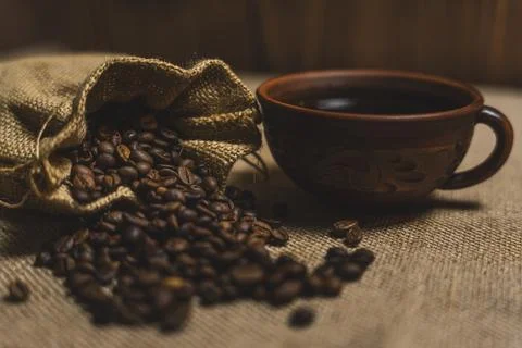 Rustic cup of black coffee with burlap sack spilling coffee beans Stock Photos