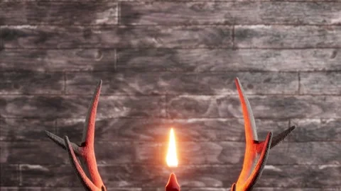 Rustic deer antlers with burning candle light against dark wooden wall. Back Stock Footage 340637525