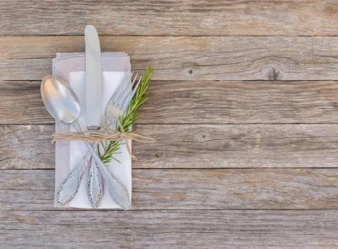 Rustic dinner menu table setting with napkin, silver cutlery and rosemary Stock Photos