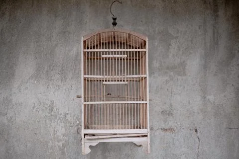 Rustic empty wooden birdcage hanging against a textured grey concrete wall. Stock Photos