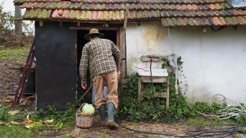 A rustic figure clad in a plaid jacket and green rubber boots carries a wicker Stock Footage 259641246