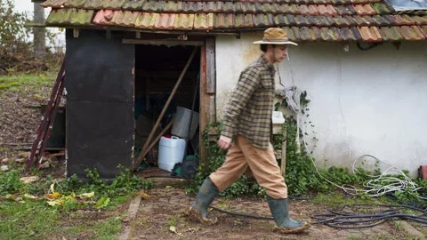 A rustic figure clad in a plaid jacket and green rubber boots carries a wicker Stock Footage 259700314