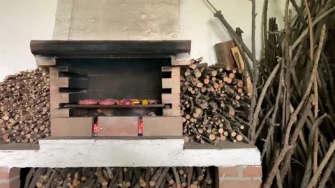 Rustic fireplace with beef grilling and large piles of chopped wood logs Видео 134609406