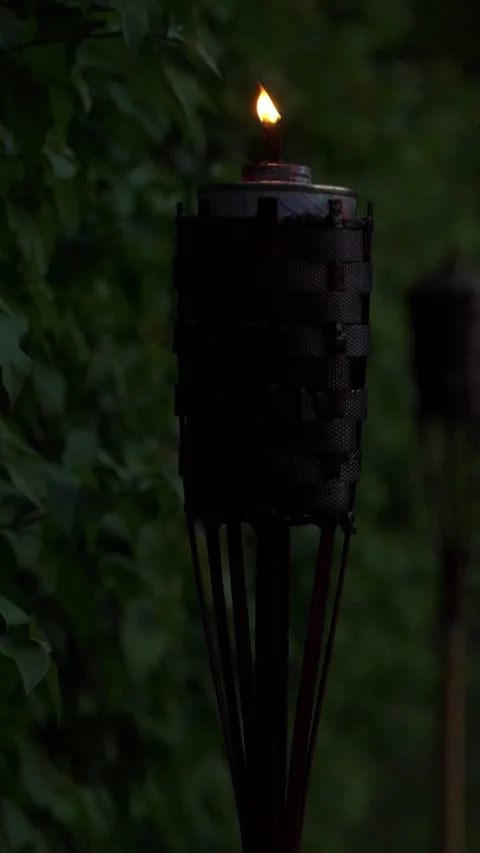 A rustic garden tiki torch burns with a small flickering flame at night Stock Footage 345137367