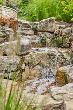 Rustic Garden Waterfall with Lush Greenery and Pebbled Pool 스톡 사진