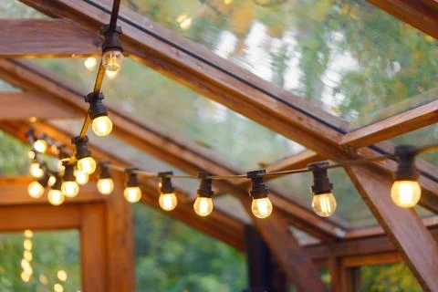 Rustic garland with lamp blulb lanterns glowing under of wooden celling, ho.. Stock Photos