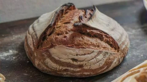 Rustic golden-brown sourdough bread loaf dusted with flour on a textured surface Stock Photos