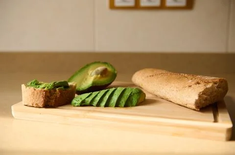 A rustic kitchen scene with avocado slices on a wooden cutting board, a halve Stock Photos
