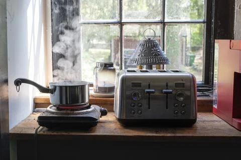 Rustic Kitchen Scene with Steaming Pot and Toaster in Sunlight. Stock Photos