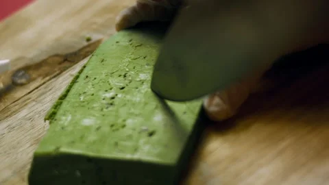 Rustic knife carving leaf points from a green cheese slice in warm light, 4K 库存影片 341109760