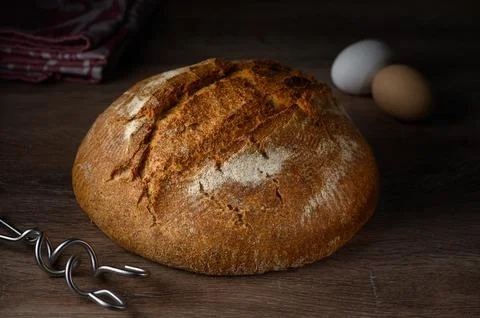 Rustic loaf of bread alongside fresh eggs on wooden countertop ready for a co Stock Photos