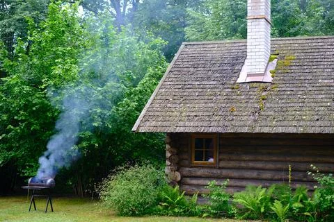 A rustic log cabin with a chimney and smoke billowing out of it. The smoke is Stock Photos