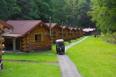Rustic log cabins in forest resort with small electric moped parked on pathway Stock Photos