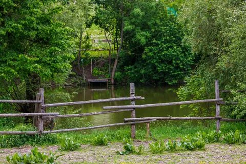 Rustic log fence in front of pond or river with small pier Stock Photos