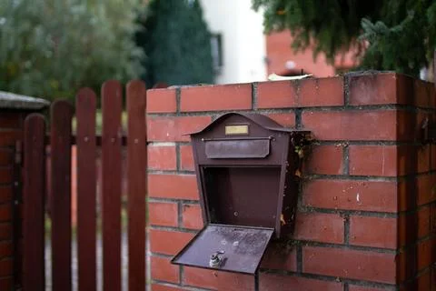 Rustic mailbox attached to a brick wall near a wooden fence in a quiet suburban Stock Photos