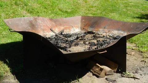 A rustic metal fire pit in a green field invites cozy gatherings Stock Footage 313986878