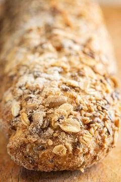 Rustic multigrain baguette topped with mixed seeds on wooden surface. Stock Photos