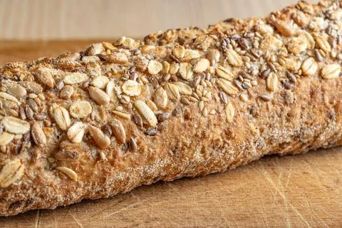 Rustic multigrain baguette topped with mixed seeds on wooden surface. Stock-Fotos