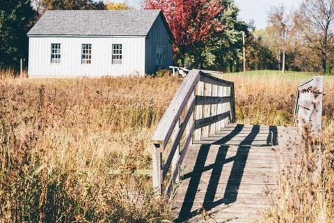 Rustic old footbridge going over a small creek in a rural area, old barn in b Stock Photos