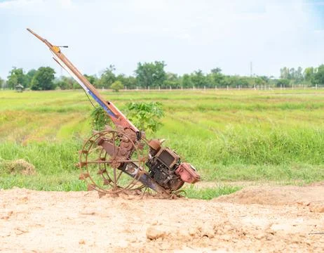 A rustic, old two-wheel walking tractor parked on a dirt pathway next to a .. Stockfoto's