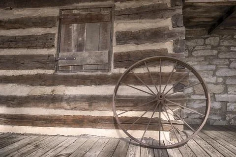 Rustic old wagon wheel leaned against a log cabin wall. Stock Photos