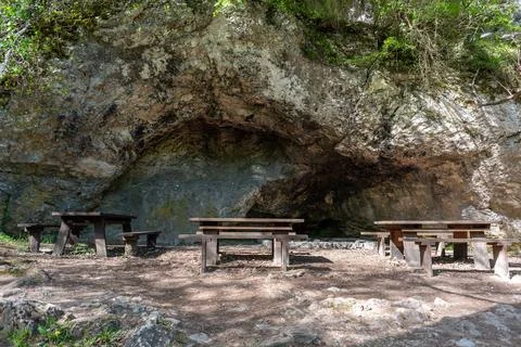 A rustic outdoor scene with a rocky backdrop featuring wooden picnic tables.. Stock Photos