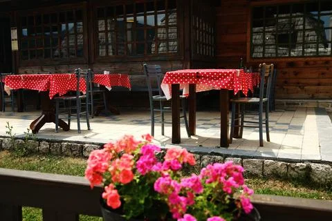 Rustic patio with red polka dot tablecloths and empty chairs, flowers in fore Stock Photos