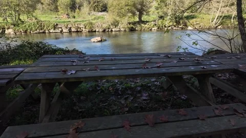 Rustic picnic table by a calm river in a forested valley Stock Footage 294697149