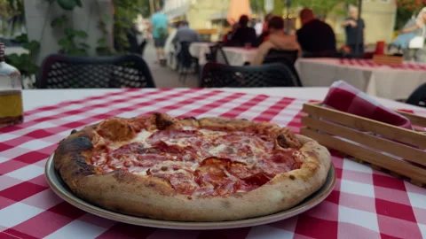 Rustic pizza on outdoor cafe table with checkered cloth and blurred diners Stock Footage 344971436