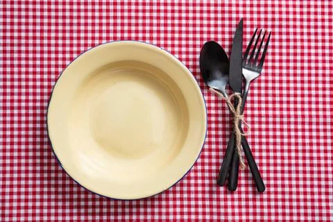 Rustic place setting. Empty enamel plate and cutlery on red checkered tablecl Foto stock