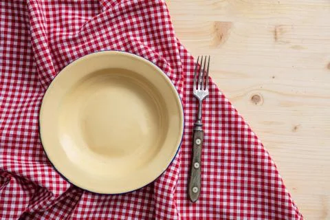 Rustic place setting. Empty enamel plate and fork, red checkered tablecloth o Stock Photos
