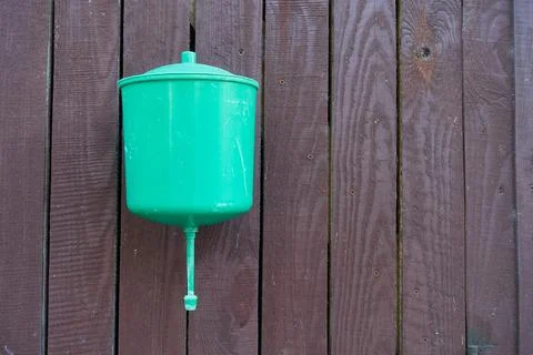 A rustic plastic open green washbasin hangs on a wooden brown wall. Stock Photos