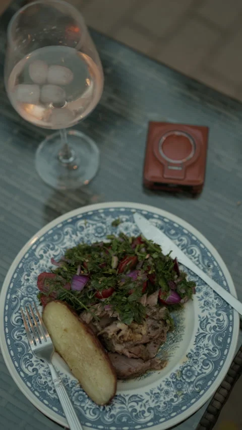 Rustic plated dinner with salad and roasted potato beside wine glass on elegant Stock Footage 345270678