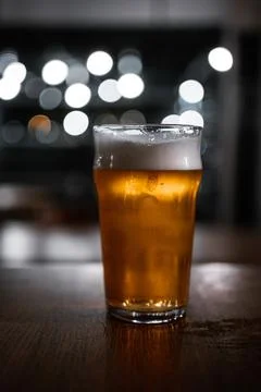 Rustic pub table with a pint of ale and bokeh light circles in the background Stock Photos