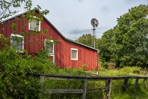 Rustic red barn with white trim, wooden fence, and old windmill Stock Photos