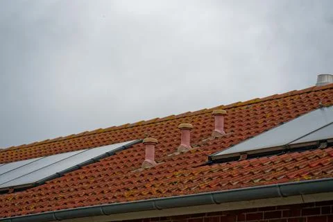 Rustic rooftop vents on red tile house with solar collectors under cloudy sky Stock Photos