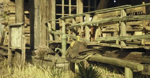 Rustic saddle resting on wooden railing near an old western building Ilustración de archivo