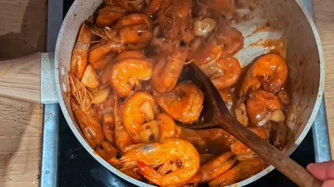 Rustic shrimp dish in vibrant orange sauce, simmering in a pan with garlic and Stock Footage 300234787