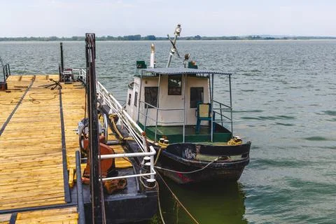 Rustic small working boat docked at a wooden pier on a calm river or lake. Stock Photos