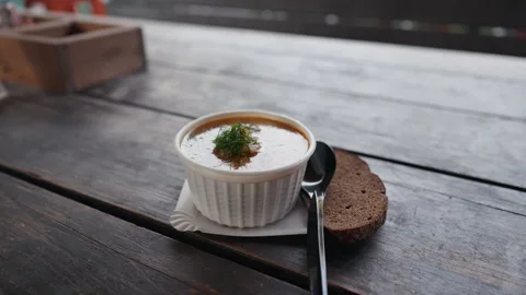 Rustic soup bowl with bread slice and spoon on dark wooden table in soft natural Stock Footage 344771045