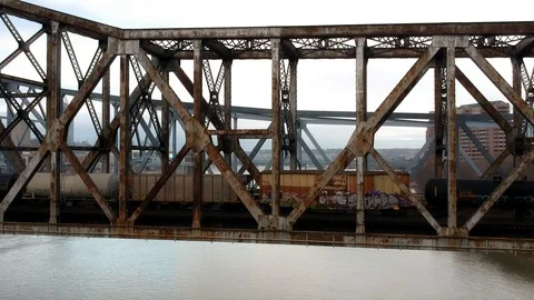 Rustic steel train bridge over river in large urban area Stock-Footage 100416496