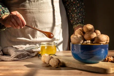 Rustic still life with honey, walnuts and woman holding wooden spoon. Stock Photos