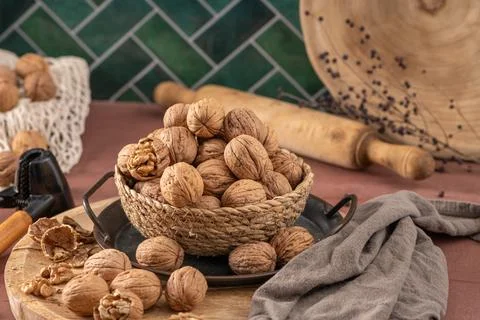 A rustic still life of whole walnuts in a woven basket on a wooden platter .. Stock Photos