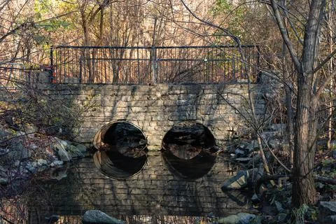 A rustic stone bridge crossing a small river with scattered rocks in an aut.. Stock Photos