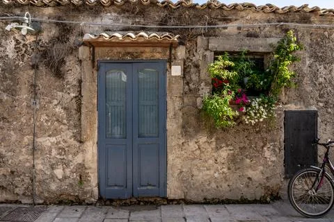 Rustic stone house facade with blue door, flower window and bicycle Fotos Stock