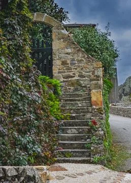 Rustic stone staircase with ivy-covered walls and black gate in southern France Stock Photos