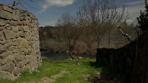 Rustic stone wall guides a dirt path towards flowing river water and trees .. Stock Footage 335461193