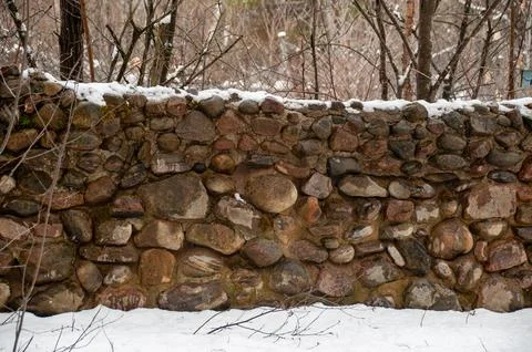 A rustic stone wall with a layer of snow in a winter forest Foto stock
