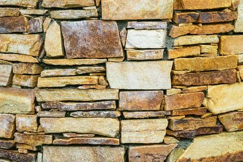 Rustic stone wall made of irregularly shaped rocks in warm earthy tones cre.. Stock Photos