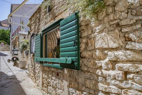 A rustic stone wall with an open green shutter frames a glimpse into a building Stock Photos